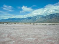 the desert in front of a large mountains is pink and gray with some clouds above