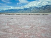 the desert in front of a large mountains is pink and gray with some clouds above