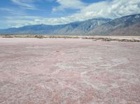 the desert in front of a large mountains is pink and gray with some clouds above