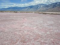 the desert in front of a large mountains is pink and gray with some clouds above