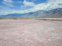 the desert in front of a large mountains is pink and gray with some clouds above