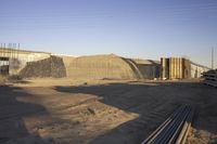 a group of pipe piles in front of a building under construction on dirt ground with metal poles nearby