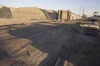 a group of pipe piles in front of a building under construction on dirt ground with metal poles nearby