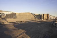 a group of pipe piles in front of a building under construction on dirt ground with metal poles nearby