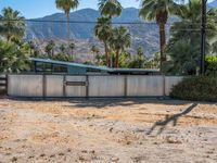 an abandoned home sits on the property in front of mountains and palm trees and a barbed fence