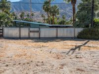 an abandoned home sits on the property in front of mountains and palm trees and a barbed fence