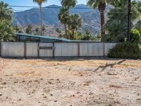 an abandoned home sits on the property in front of mountains and palm trees and a barbed fence