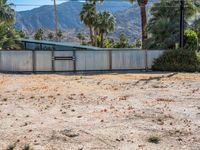 an abandoned home sits on the property in front of mountains and palm trees and a barbed fence