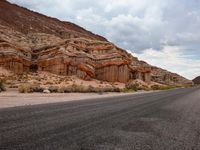 an empty road in the middle of a mountainous area with orange rock walls in the background