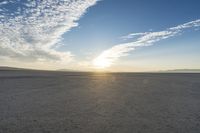 the sky is filled with clouds and sun going down in a barren plain area,