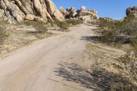 a dirt road between two large boulders and shrubs near some bushes and rocks in the desert