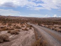 an open dirt road in the middle of the desert, with a car parked on either side