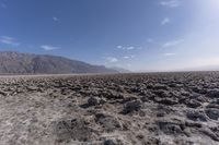 a field that has rocks and dirt on the ground in it with mountains in the distance