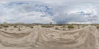 an open sand field with dunes in the background and cloudy sky above it during daytime