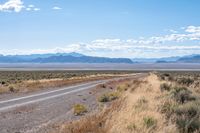 a long highway running through the desert with mountains in the background behind it with clouds