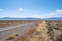 a long highway running through the desert with mountains in the background behind it with clouds