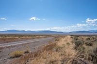 a long highway running through the desert with mountains in the background behind it with clouds