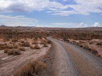 a small dirt road leading across the desert from a hill to a large hill behind it