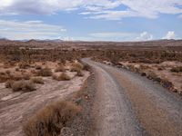 a small dirt road leading across the desert from a hill to a large hill behind it