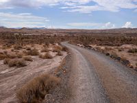 a small dirt road leading across the desert from a hill to a large hill behind it