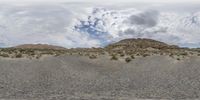 a desert landscape with a hill in the background and clouds in the sky above it