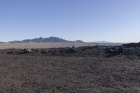 a lone mountain covered with rocks and rubble in the middle of nowhere landscape with mountains on the far horizon