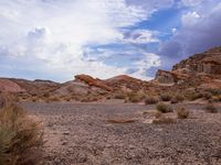 there is a desert area with some bushes and rocks on the ground in it and clouds