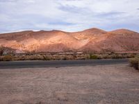 an empty desert with hills in the background and a truck on the side of the road