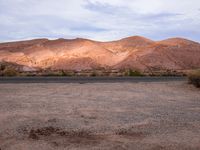 an empty desert with hills in the background and a truck on the side of the road