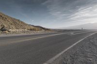 a lone motorcycle driving down the road on a sunny day from the mountains to the horizon