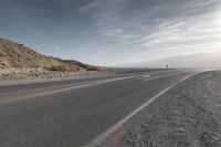 a lone motorcycle driving down the road on a sunny day from the mountains to the horizon