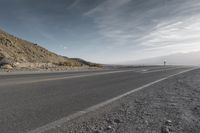 a lone motorcycle driving down the road on a sunny day from the mountains to the horizon