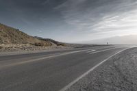 a lone motorcycle driving down the road on a sunny day from the mountains to the horizon