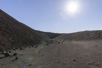 the sun rises over a desert with rocks and dirt on it a person is walking across the grass