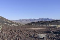 a lone sign sits among the rocks on the desert hill side in front of a mountain range