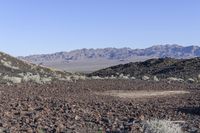 a lone sign sits among the rocks on the desert hill side in front of a mountain range