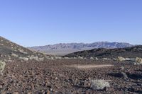 a lone sign sits among the rocks on the desert hill side in front of a mountain range