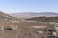 a lone sign sits among the rocks on the desert hill side in front of a mountain range