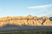 a mountain range in the desert in front of some distant mountains and blue sky below