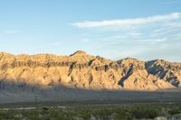 a mountain range in the desert in front of some distant mountains and blue sky below