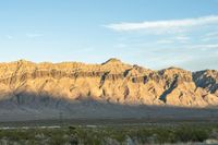 a mountain range in the desert in front of some distant mountains and blue sky below