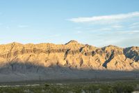 a mountain range in the desert in front of some distant mountains and blue sky below