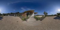 a fisheye view of a nice modern house in a desert climate setting, and shows the driveway and entry way