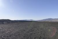 a lone motorcycle is traveling through a large field of dirt, with mountains in the distance