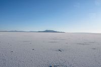 a lone white vehicle on a salt plain with mountains in the background in the foreground