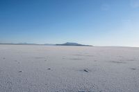 a lone white vehicle on a salt plain with mountains in the background in the foreground