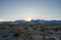 the sun setting over a large mountain range in the desert in front of power lines