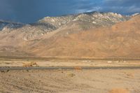 a lone white truck sitting on top of a desert next to a mountain range under cloudy skies