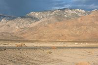 a lone white truck sitting on top of a desert next to a mountain range under cloudy skies