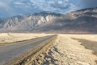 an empty road in front of a mountain range and dry, brown landscape with snow on it